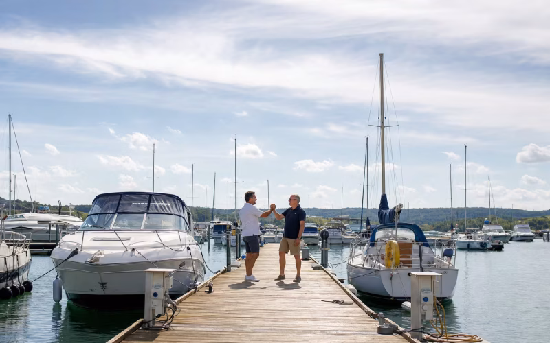 Zwei Bootsfahrer begrüßen sich freundlich per Handschlag auf einem Steg in einer sonnigen Marina