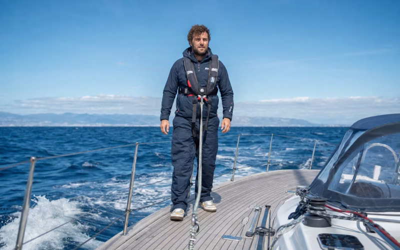Segler trägt eine moderne automatische Rettungsweste mit Lifebelt an Deck einer Segelyacht auf See