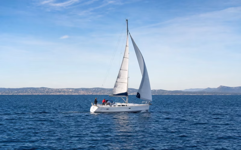Segelyacht mit Crew bei einem Wendemanöver auf blauem Wasser vor einer Küste