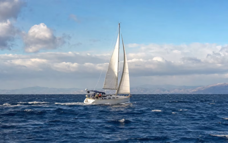 Segelyacht segelt bei frischem Wind mit verkleinerter Segelfläche über blaues Meer mit Schaumkronen