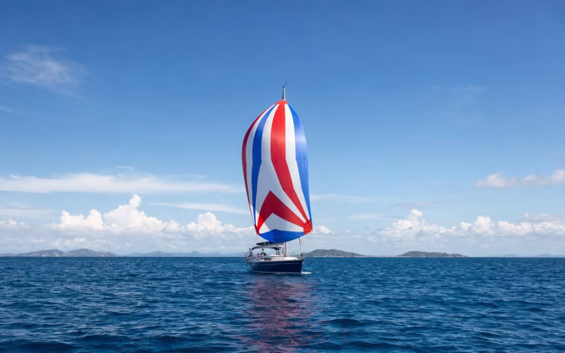 Segelyacht läuft unter einem großen bunten Gennaker vor dem Wind über blaues Meer