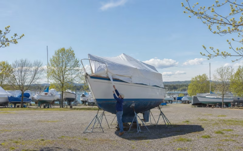 Person nimmt im Frühjahr die Winterabdeckung von einem Segelboot im sonnigen Bootslager