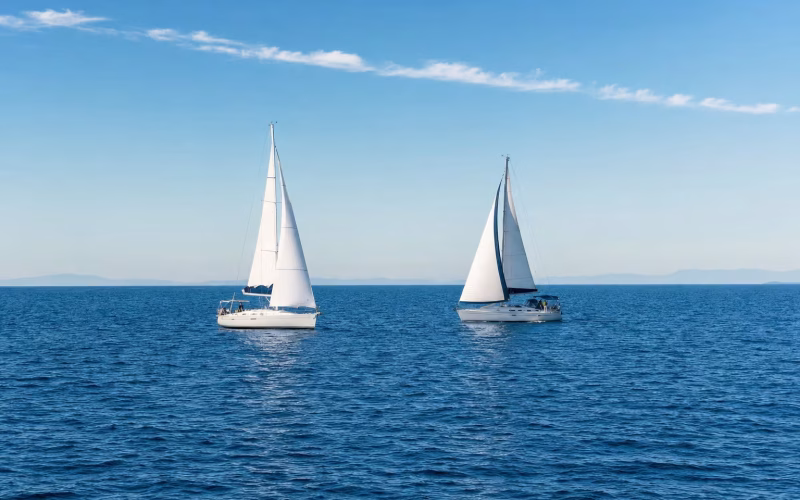 Zwei Segelyachten auf kreuzenden Kursen auf offenem Wasser unter klarem Himmel