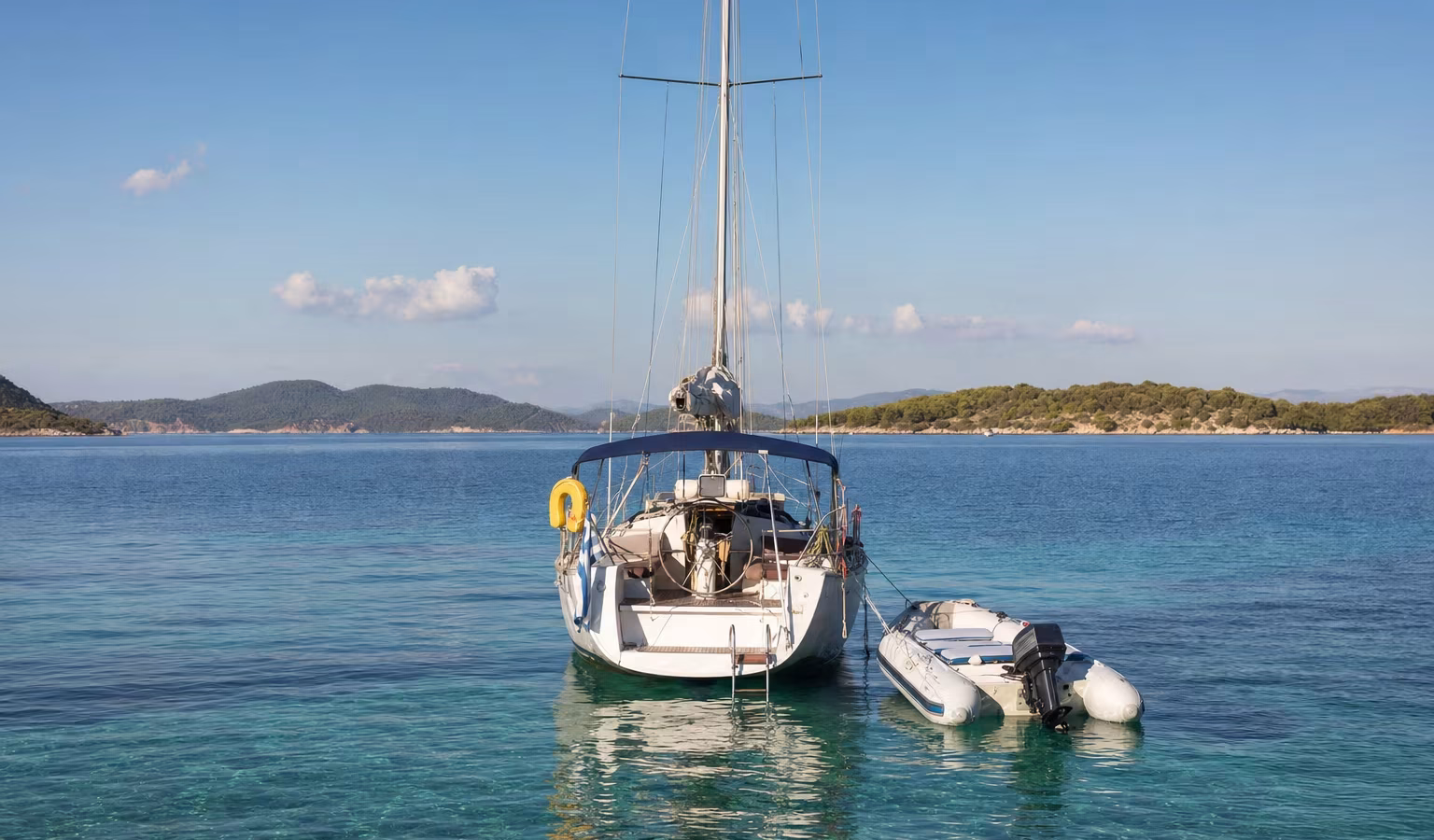 Schlauchboot mit kleinem Außenborder am Heck einer ankernden Segelyacht in einer Bucht