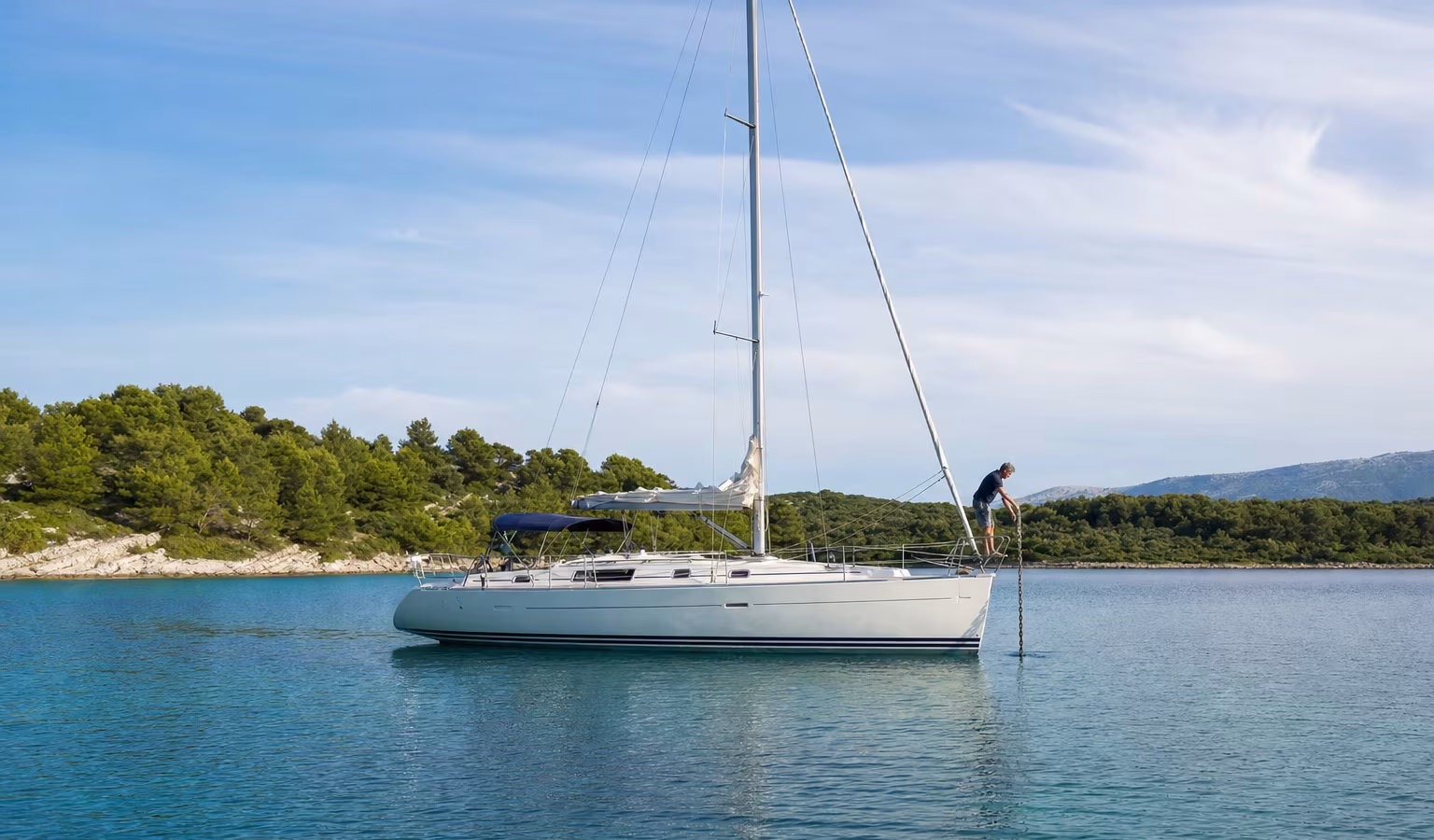 Segelyacht lässt in einer geschützten Bucht den Anker fallen, ein Crewmitglied am Bug