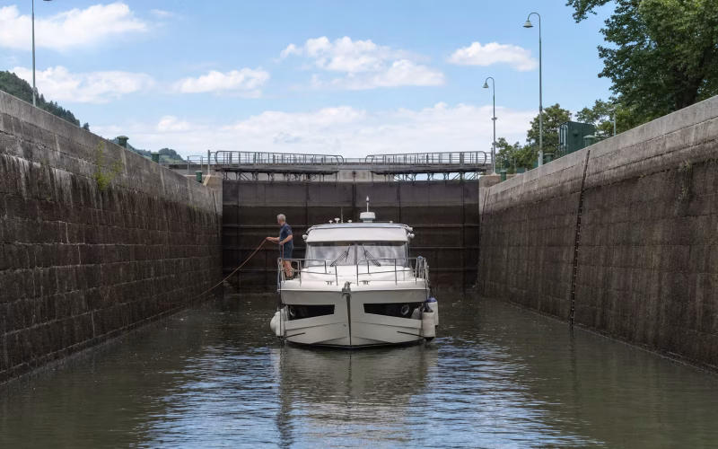 Motorboot in einer Kanalschleuse mit hohen Schleusenwänden, ein Crewmitglied hält die Leine