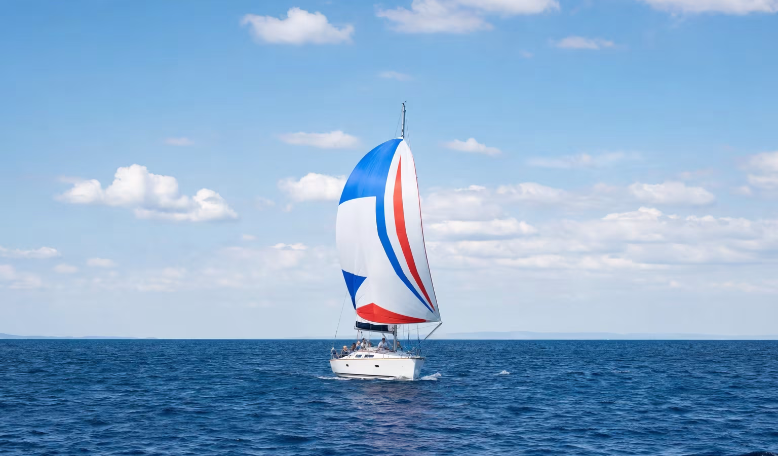 Segelyacht unter buntem Gennaker bei raumem Wind und Sonne