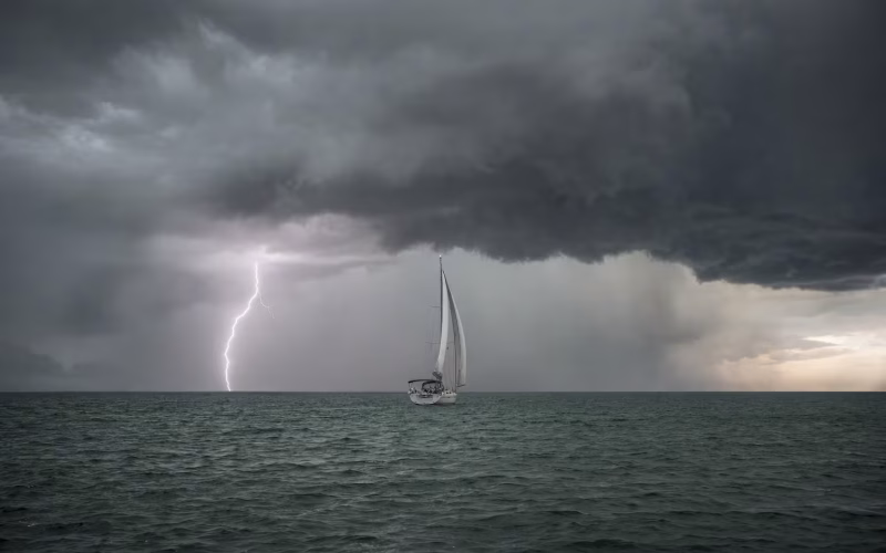 Dunkle Gewitterfront mit Blitz über offener See, Segelyacht in der Ferne