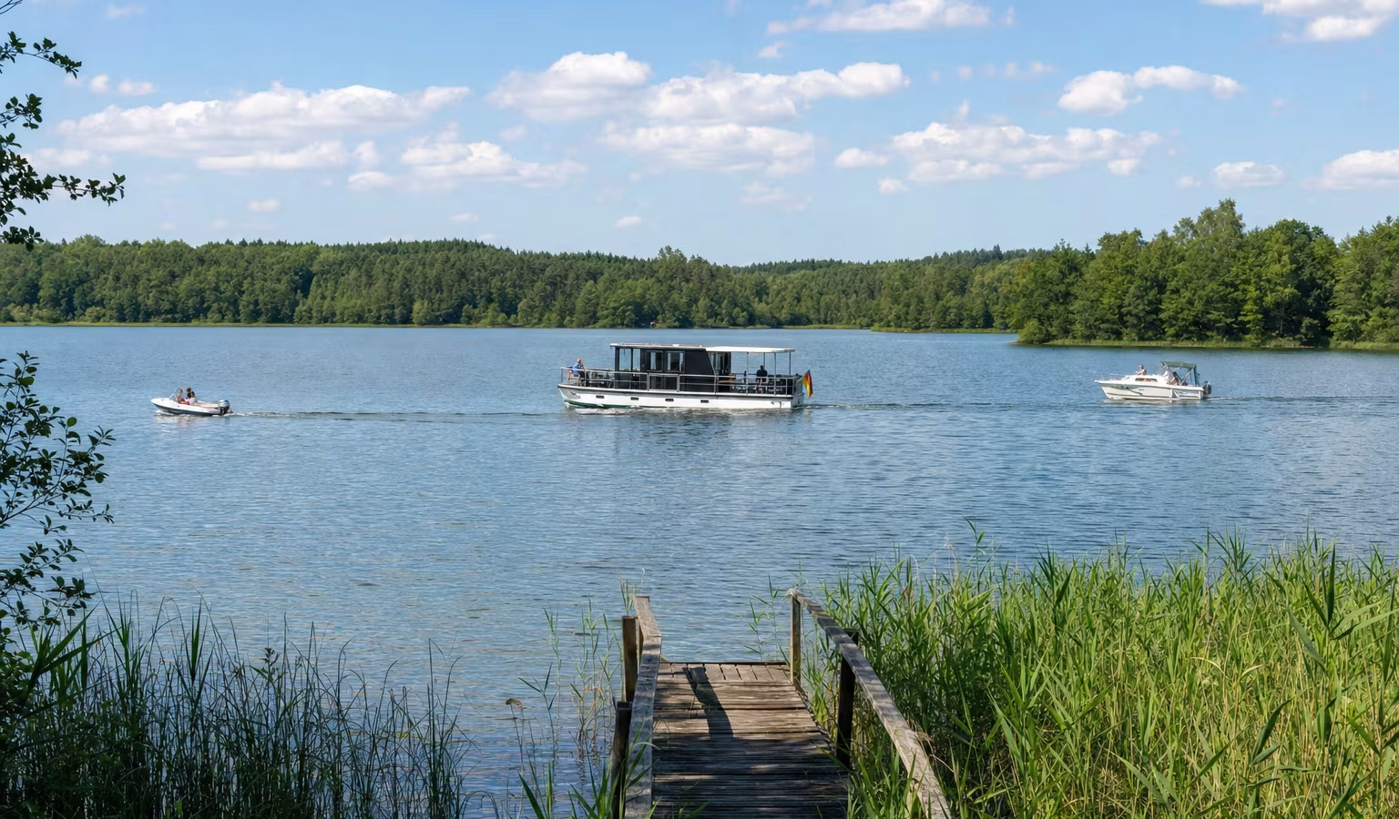 Hausboot und Motorboote auf einem stillen See der Mecklenburgischen Seenplatte