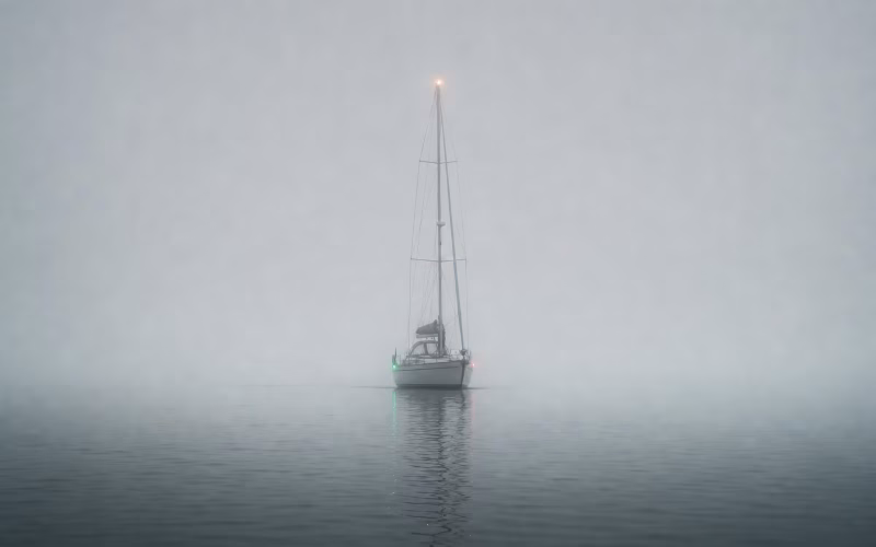 Segelyacht mit brennenden Positionslampen gleitet durch dichten grauen Nebel auf ruhigem Wasser